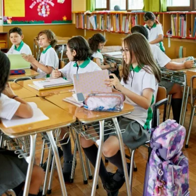 Sala de clases en Chile: estudiantes de uniforme en pupitres, pizarra de Matemática al fondo.